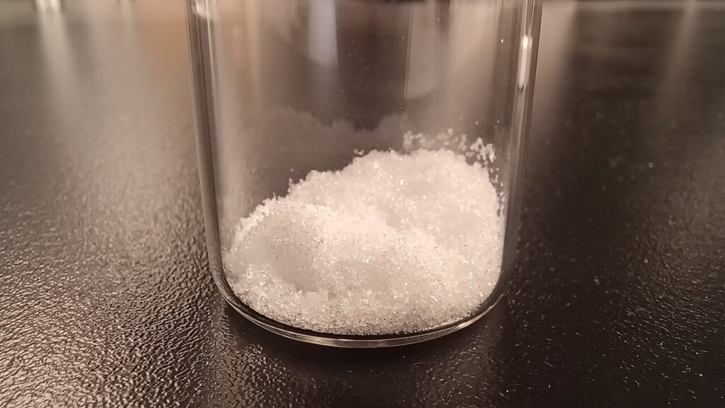 투명한 유리 용기 바닥에 모인 흰색 글라이콜릭애씨드 결정